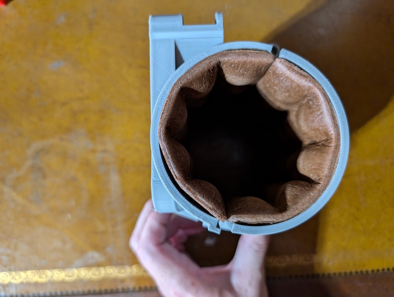 May include: A gray 3D printed cup holder with a brown leather lining.