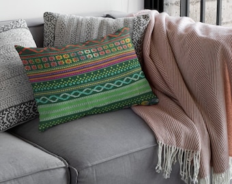 Puede incluir: Una almohada verde con un patrón geométrico colorido. La almohada está en un sofá gris con una manta de tiro rosa.