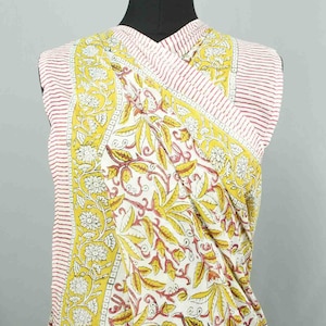 Puede incluir: Un top sin mangas envolvente con un estampado floral. La tela presenta un fondo blanco con dise&ntilde;os bot&aacute;nicos amarillos y rojos. Los bordes tienen rayas rojas y blancas.
