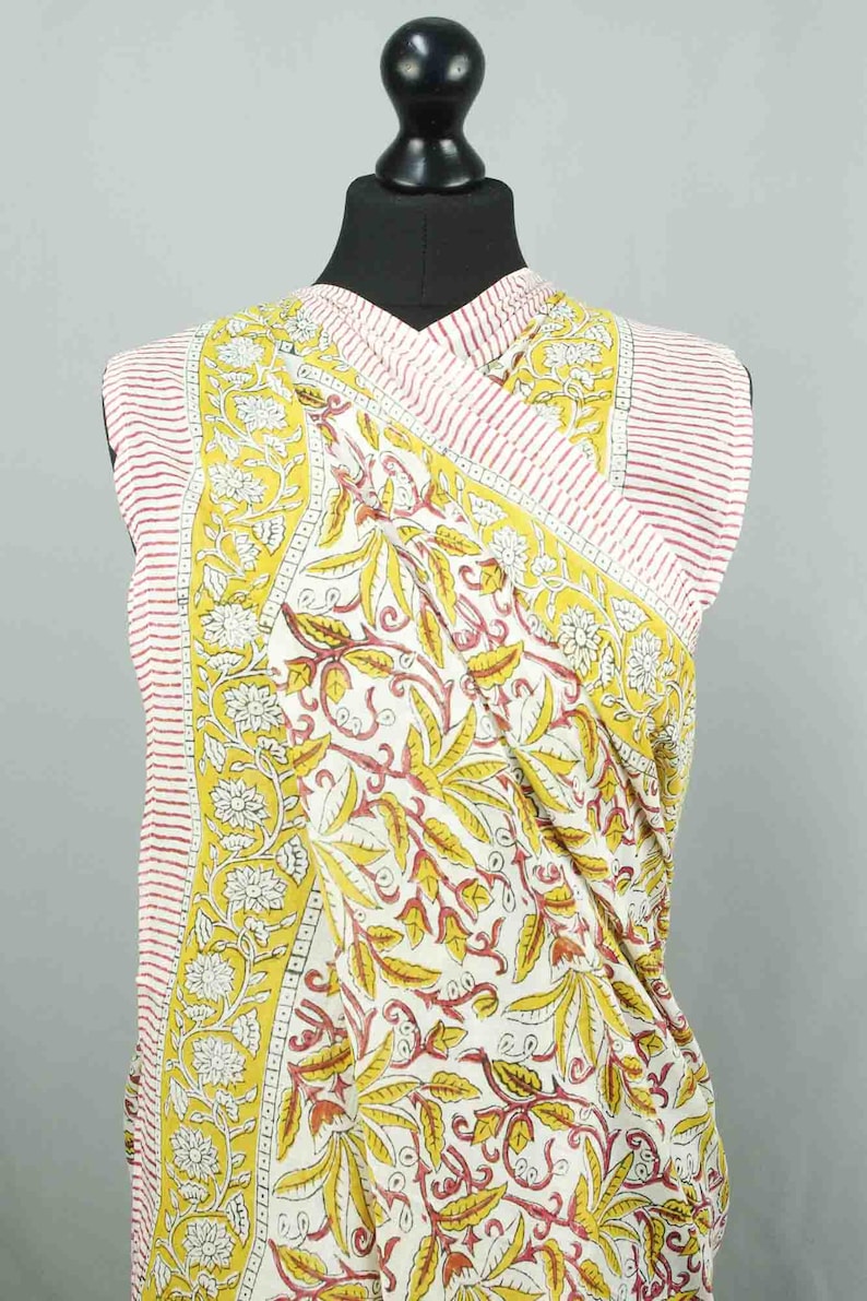 Puede incluir: Un top sin mangas envolvente con un estampado floral. La tela presenta un fondo blanco con dise&ntilde;os bot&aacute;nicos amarillos y rojos. Los bordes tienen rayas rojas y blancas.
