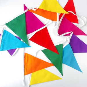 Puede incluir: Un banderín colorido con banderas triangulares en tonos de rojo, naranja, amarillo, verde, azul, morado y rosa. Las banderas están cosidas juntas con tela blanca.