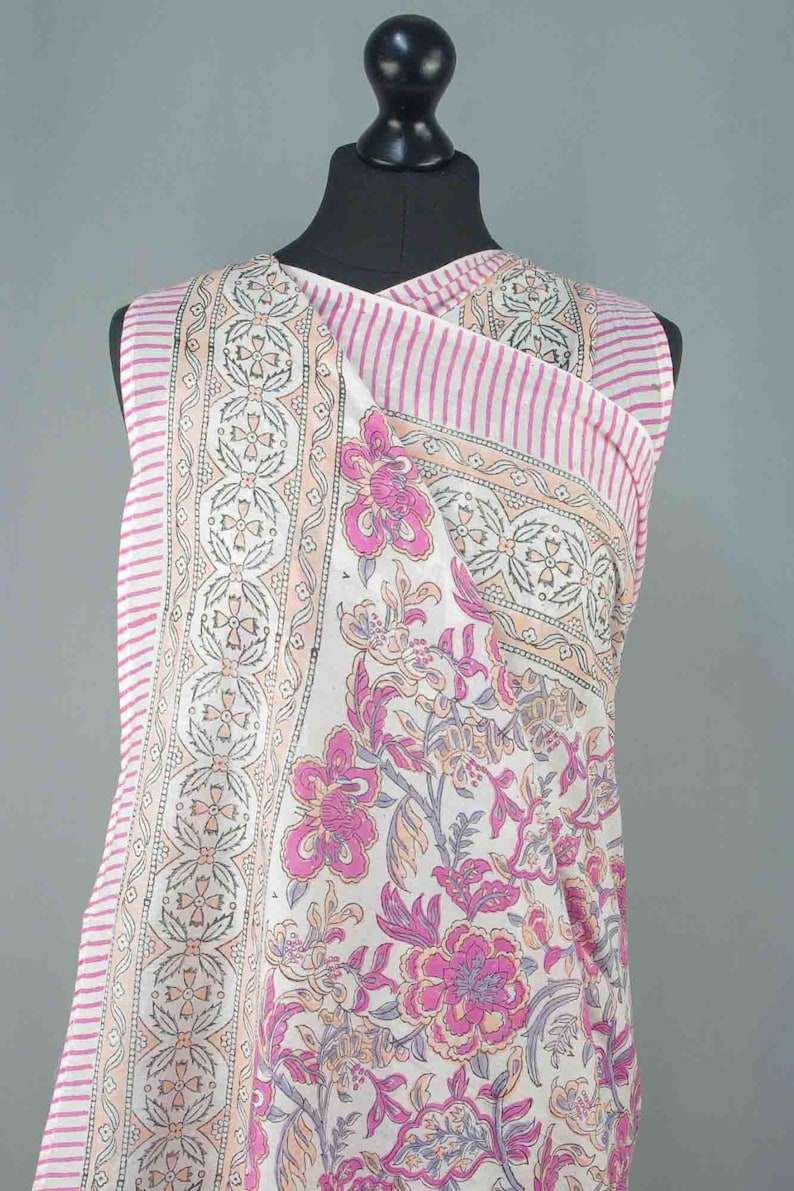 Puede incluir: Una prenda sin mangas, estilo envolvente, con un estampado floral y a rayas. La tela presenta una base blanca con dise&ntilde;os florales rosas y melocot&oacute;n, acentuados por rayas rosas. La prenda se exhibe en un maniqu&iacute; negro.