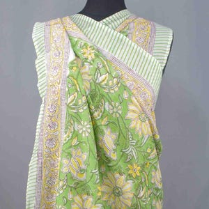 Puede incluir: Textil verde con estampado floral drapeado sobre un maniqu&iacute;. La tela presenta grandes flores amarillas y hojas verdes sobre un fondo verde claro. El borde tiene un patr&oacute;n de rayas con acentos amarillos y morados.