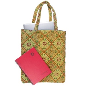 May include: A yellow tote bag with a geometric pattern in green and red, holding a silver laptop. A red spiral-bound notebook with the text "A5 Notebook" is in front of the bag. The bag has matching handles.