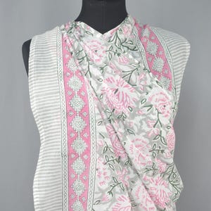 Puede incluir: Una tela a rayas blancas y grises con una bufanda floral drapeada sobre ella. La bufanda presenta un estampado floral rosa con hojas verdes y un borde rosa con dise&ntilde;os geom&eacute;tricos. La tela se exhibe en un maniqu&iacute; negro.