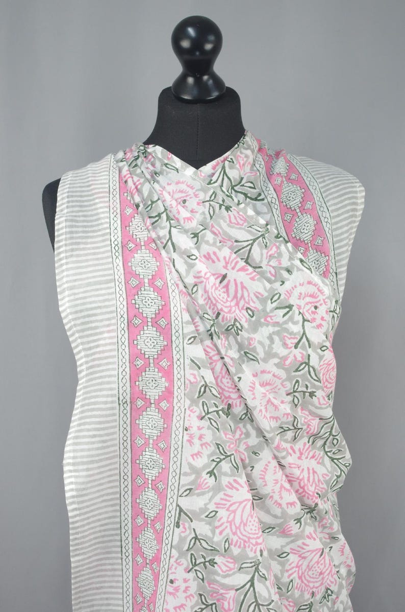 Puede incluir: Una tela a rayas blancas y grises con una bufanda floral drapeada sobre ella. La bufanda presenta un estampado floral rosa con hojas verdes y un borde rosa con dise&ntilde;os geom&eacute;tricos. La tela se exhibe en un maniqu&iacute; negro.