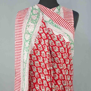 Puede incluir: Textil a rayas rojas y blancas con un estampado floral. El textil est&aacute; drapeado sobre un maniqu&iacute;. El textil tiene un fondo rojo con un estampado floral verde repetido. Los bordes tienen un borde floral blanco y verde.