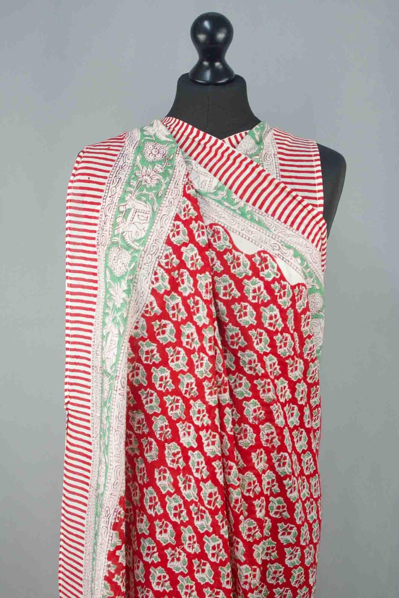 Puede incluir: Textil a rayas rojas y blancas con un estampado floral. El textil est&aacute; drapeado sobre un maniqu&iacute;. El textil tiene un fondo rojo con un estampado floral verde repetido. Los bordes tienen un borde floral blanco y verde.