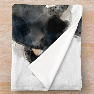 May include: A soft, white fleece throw blanket with a black and gray watercolor design. The design features abstract shapes and splatters of paint.
