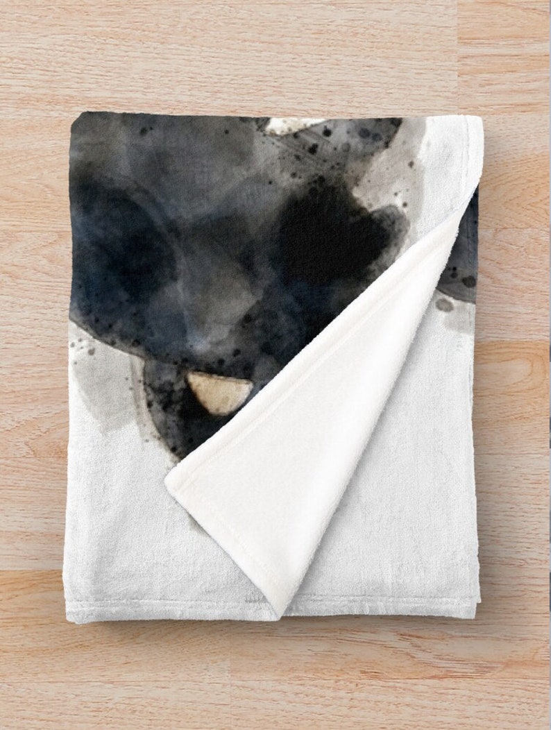 May include: A soft, white fleece throw blanket with a black and gray watercolor design. The design features abstract shapes and splatters of paint.