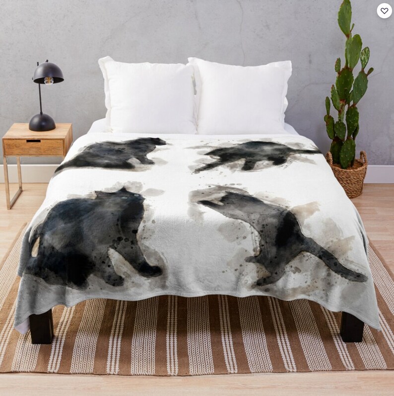 May include: A white throw blanket with a watercolor design of four black cats in different poses. The cats are painted in a loose, abstract style with splashes of gray and brown.