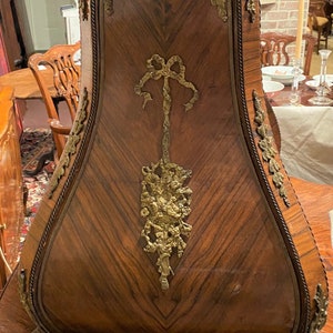 Puede incluir: Un gabinete de madera con una parte superior curva y adornada y detalles intrincados de lat&oacute;n. El gabinete est&aacute; hecho de madera oscura con un patr&oacute;n de chevron y presenta un lazo de lat&oacute;n decorativo y un dise&ntilde;o floral.
