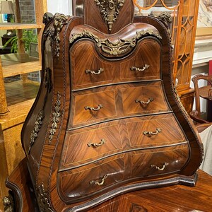 Puede incluir: Un arc&oacute;n de cajones de madera curvado con detalles de lat&oacute;n ornamentados y una tapa decorativa. El arc&oacute;n tiene seis cajones con tiradores de lat&oacute;n y est&aacute; hecho de madera oscura con un dise&ntilde;o de marqueter&iacute;a.