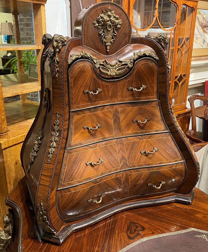 Puede incluir: Un arc&oacute;n de cajones de madera curvado con detalles de lat&oacute;n ornamentados y una tapa decorativa. El arc&oacute;n tiene seis cajones con tiradores de lat&oacute;n y est&aacute; hecho de madera oscura con un dise&ntilde;o de marqueter&iacute;a.