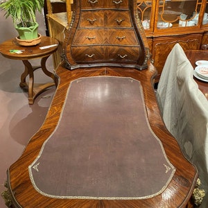 Puede incluir: Un escritorio de madera vintage con una tapa de cuero marr&oacute;n y una secci&oacute;n superior curvada y adornada con varios cajones. El escritorio tiene una rica veta de madera y detalles intrincados.