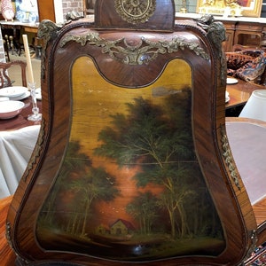 Puede incluir: Un gabinete de madera vintage con una escena pintada de un bosque con una peque&ntilde;a casa. El gabinete tiene adornos de lat&oacute;n ornamentados y una parte superior curva.