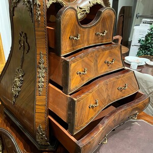 Puede incluir: Una c&oacute;moda antigua de madera con tallas intrincadas y detalles en lat&oacute;n. La c&oacute;moda tiene cuatro cajones con frentes curvos y tiradores ornamentados. Los cajones est&aacute;n abiertos, revelando la veta de la madera y el interior de la c&oacute;moda.