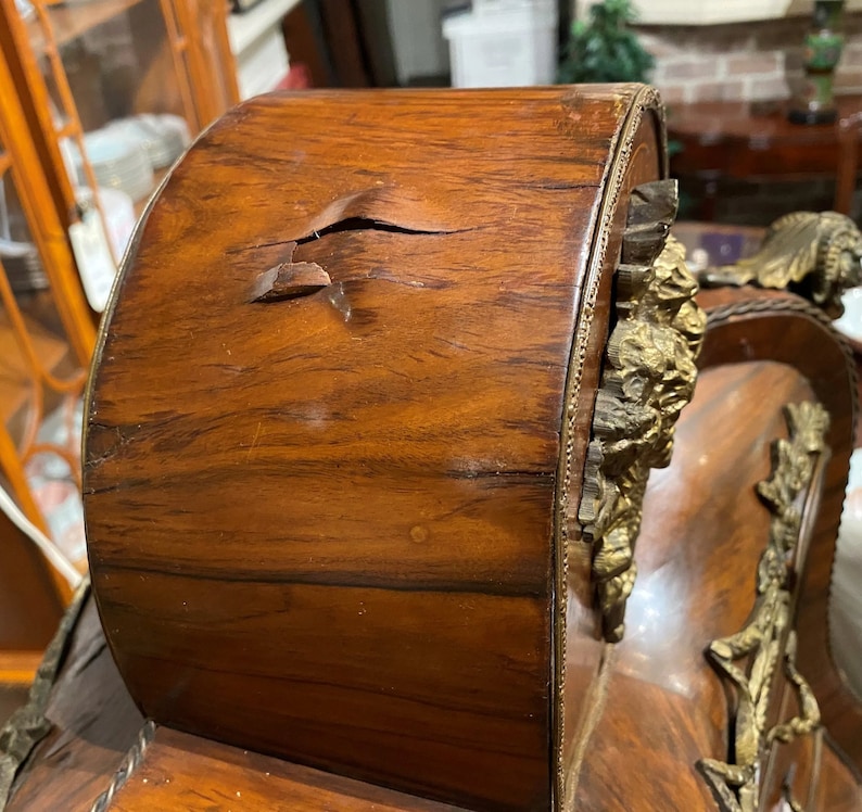 Puede incluir: Un reloj antiguo de madera con adornos dorados y una grieta en la madera. El reloj necesita ser reparado.