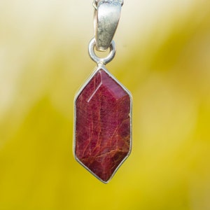 May include: A silver pendant with a red gemstone in a hexagonal shape.