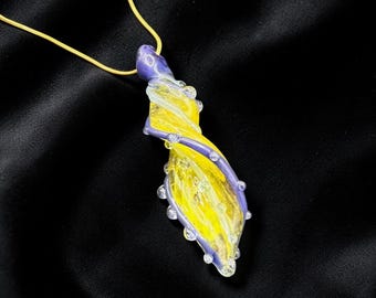 May include: A handcrafted glass pendant necklace with a twisted design. The pendant features yellow and purple hues, accented with clear, round embellishments. The necklace has a delicate gold chain, perfect for adding a touch of elegance to any outfit.