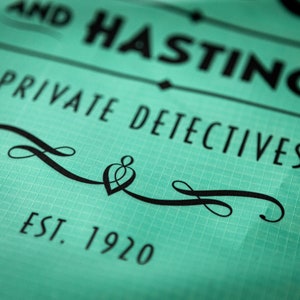 May include: A teal green sign with black text that reads "AND HASTINGS PRIVATE DETECTIVES EST. 1920". The sign has a decorative black flourish with a heart shape in the center.