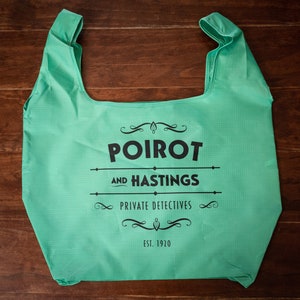 May include: A green reusable shopping bag with the text "POIROT AND HASTINGS PRIVATE DETECTIVES EST. 1920" printed on it.