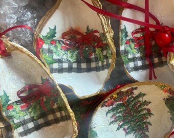 May include: Several oyster shell ornaments with gold edges and red ribbon hangers. The shells are decorated with Christmas-themed designs, including holly, red bows, and a black and white checkered pattern.