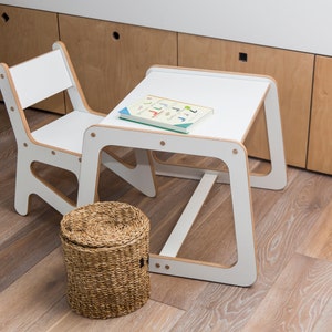 May include: White children's table and chair set with a woven storage basket. The table has a white top and white legs. The chair has a white seat and white legs. The storage basket is brown and woven.