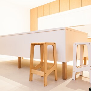 May include: Two wooden step stools in a kitchen setting. One stool is natural wood and the other is white.