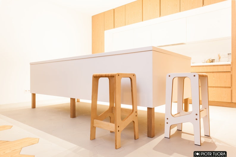 May include: Two wooden step stools in a kitchen setting. One stool is natural wood and the other is white.