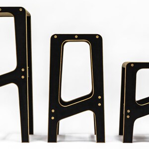 May include: Three black wooden stools with gold accents. The stools are different sizes, with the largest stool at the back and the smallest stool at the front.