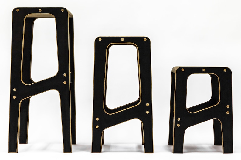 May include: Three black wooden stools with gold accents. The stools are different sizes, with the largest stool at the back and the smallest stool at the front.