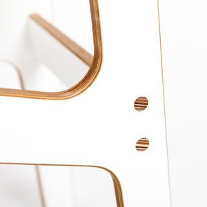 May include: White plywood chair with rounded edges and two visible holes. The chair is made of wood with a natural wood grain.