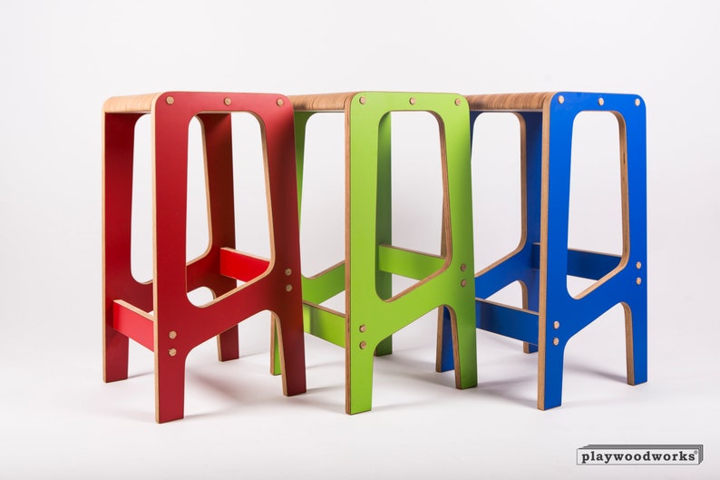 May include: Three wooden step stools in red, green, and blue. The stools are made of plywood and have a simple, modern design.  The stools are all the same size and shape, but they are painted in different colours.  The stools are arranged in a row, with the red stool on the left, the green stool in the middle, and the blue stool on the right.  The stools are all standing on a white surface.  The text "playwoodworks" is visible in the bottom right corner of the image.