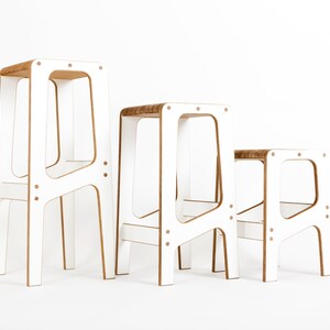 May include: Three white wooden stools of varying heights. The stools have a simple, modern design with a rectangular seat and four legs.
