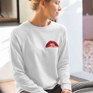 Peut inclure: Sweat-shirt blanc avec un motif rouge et blanc d'une bouche avec des dents sur le devant.