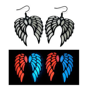 May include: A pair of black metal wing-shaped earrings with a white inner design. The earrings are shown with a glowing effect in red and blue, suggesting a glow-in-the-dark feature. The earrings have a hook closure.