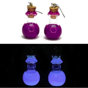 May include: A pair of potion bottle earrings. Each glass bottle is filled with a vibrant purple liquid and topped with a cork. The earrings have silver-colored ear wires. The bottom image shows the earrings glowing blue in the dark.