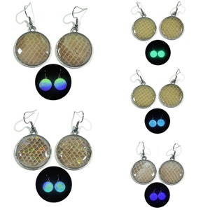 May include: A pair of silver earrings with round, beige, textured resin pendants. The earrings glow in the dark, with a blue-green glow.