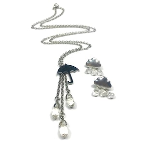 May include: A silver-toned necklace featuring a small umbrella charm with three dangling clear crystal teardrop beads, accompanied by a pair of matching stud earrings, each shaped like a silver cloud with three small clear crystal drops.
