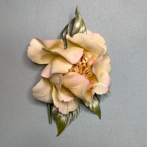 May include: A delicate, pale pink and cream colored fabric flower with green leaves. The flower is made to look like a peony.