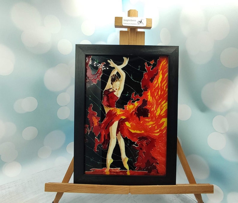 May include: Framed stained glass artwork depicting a dancer in a red dress with a fiery orange background.