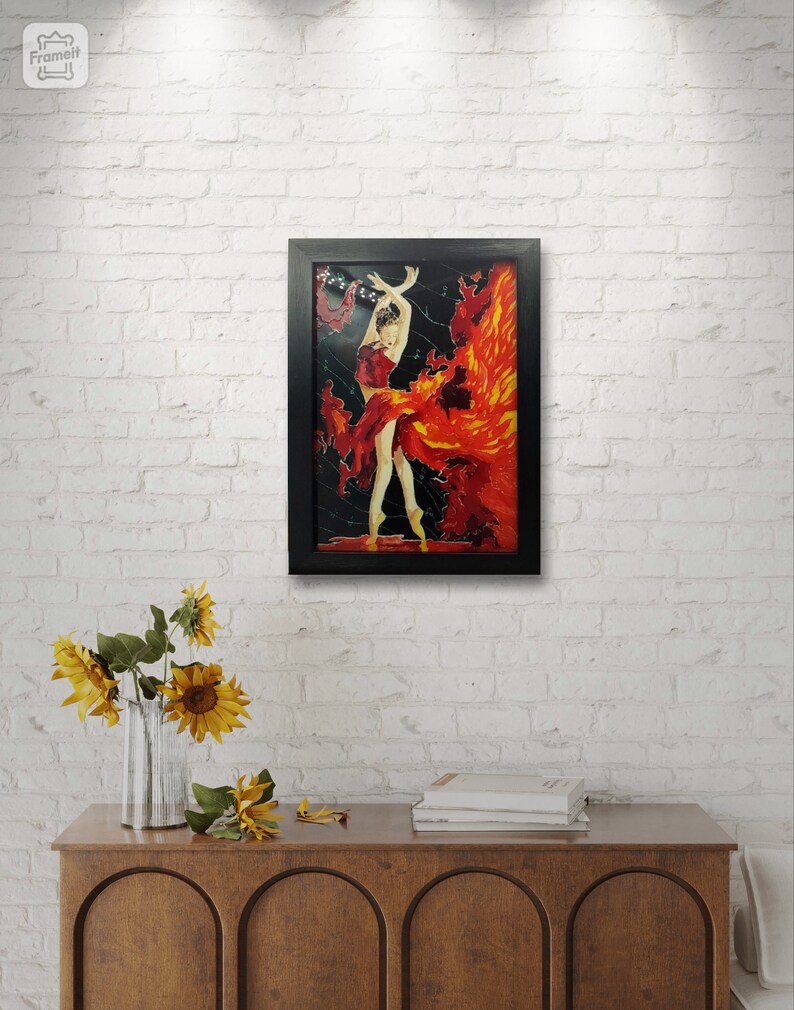 May include: A framed painting of a woman in a red dress dancing with a fiery background. The painting is set against a white brick wall.