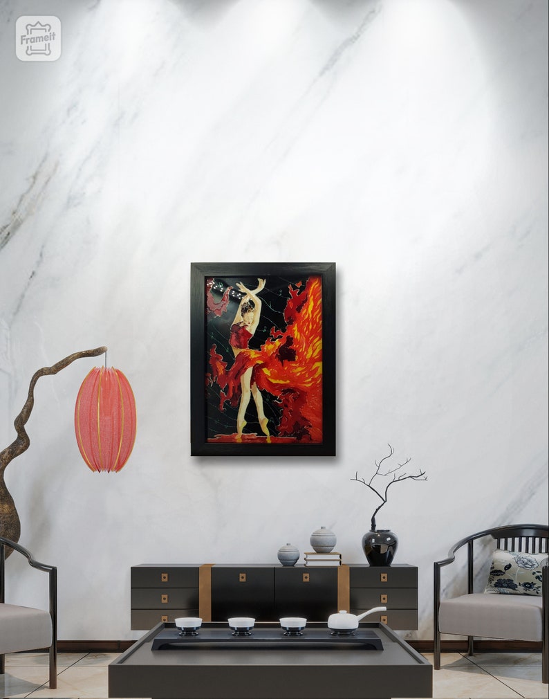 May include: A framed painting of a woman in a red dress dancing with flames behind her. The painting is set against a white marble wall with a black frame.