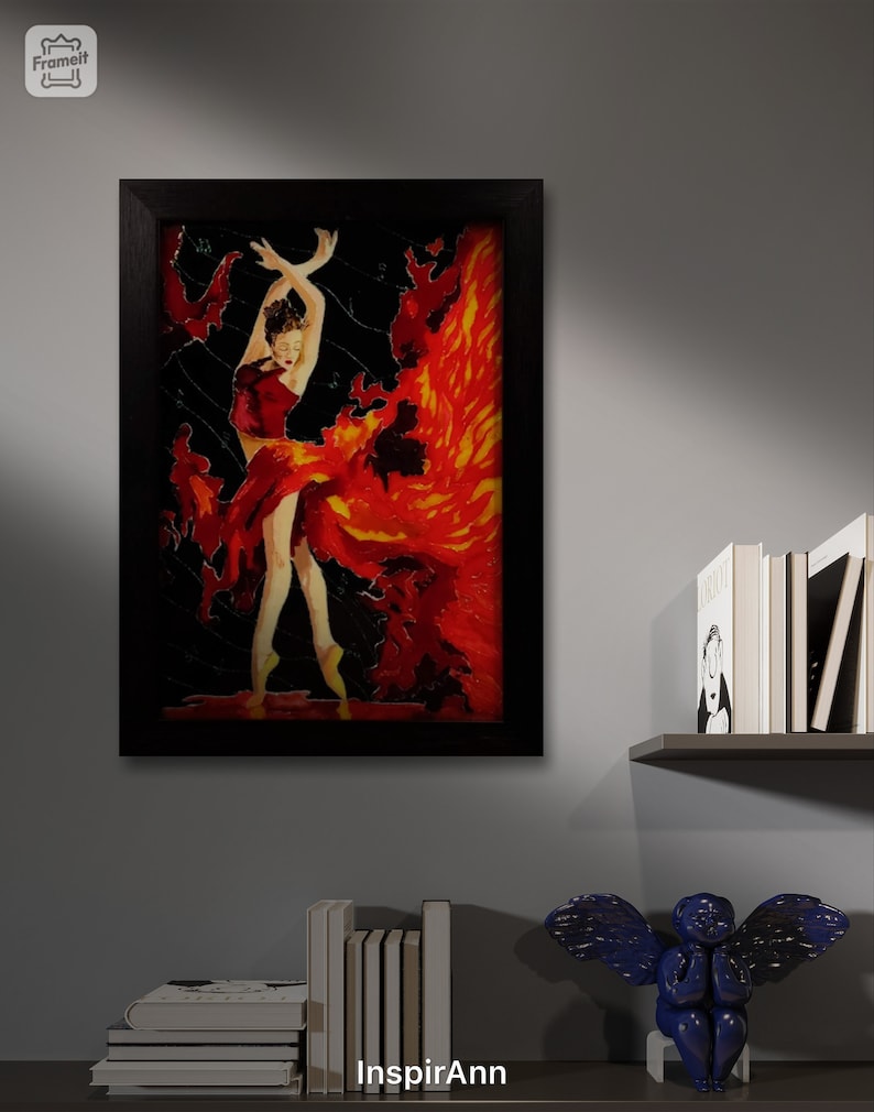 May include: A framed painting of a woman in a red dress with a fiery orange and yellow background. The woman is dancing with her arms raised above her head. The painting is set against a gray wall with a shelf of books and a blue angel figurine.