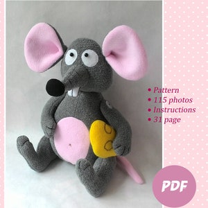 May include: A gray and pink plush mouse toy holding a yellow cheese wedge. The toy is sitting on a pink background with white polka dots. The text "Master Class "Mouse Cracker"  • Pattern • 115 photos • Instructions • 31 page PDF Author's pattern Olga Razuvaeva" is visible in the image.