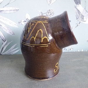 Può includere: Un saliera in ceramica marrone con una glassa gialla e un design decorativo. Il saliera è inclinato di lato, e la parola "Sale" è visibile sul fondo.