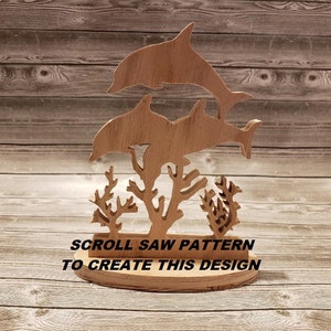 May include: Wooden scroll saw pattern of two dolphins jumping over coral. The text "SCROLL SAW PATTERN TO CREATE THIS DESIGN" is below the dolphins.