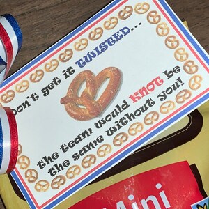 May include: A white card with red and blue borders and a pretzel image. The card reads "Don't get it twisted... the team would knot be the same without you!"