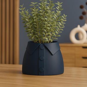 May include: A navy blue ceramic planter shaped like a collared shirt, with three button details. The planter is filled with green leafy plants. The design is modern and unique, suitable for home decor.